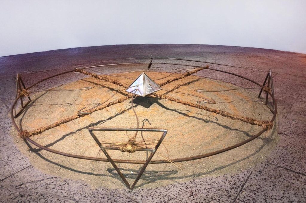 Gira X, Installation, 2024. Acier, lianes, terre noire et rouge. Sculpture, 120 x 120 cm. Pliage, soudure et ligature.